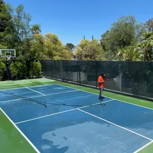 Cleaning the siding fence on a tennis court with a power washer hose